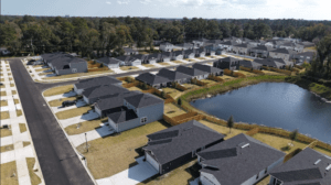 Aerial view of a suburban neighborhood with rows of gray-roofed houses surrounding a man-made pond.